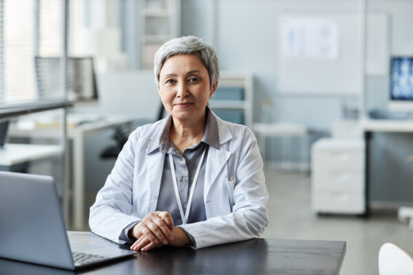 Experienced female doctor sitting at desk using laptop