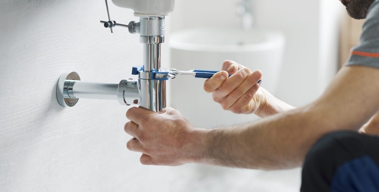Someone using a wrench on the drain under a sink