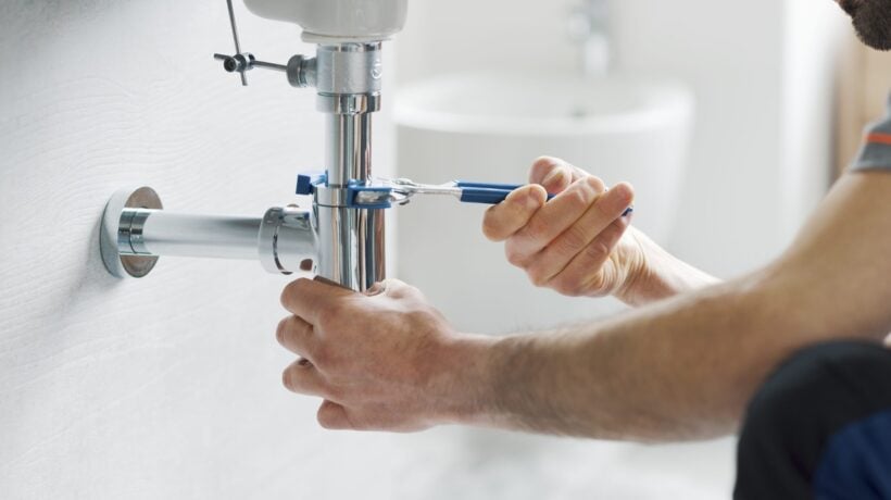 Someone using a wrench on the drain under a sink